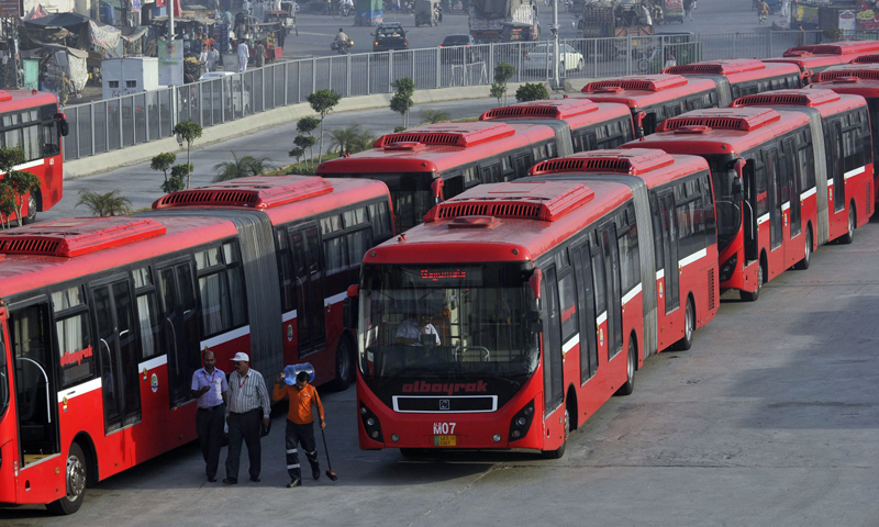 Description: This photograph taken on June 5, 2013, shows employees walking beside metro buses parked at a terminal in Lahore. &mdash; AFP Photo