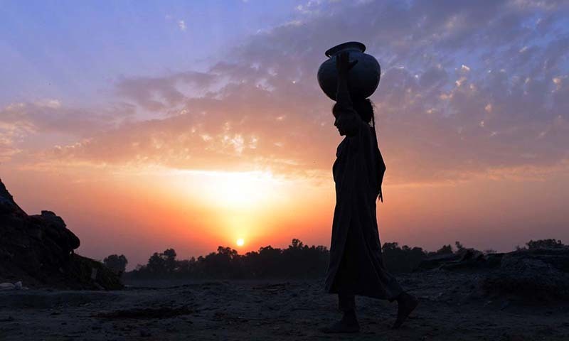 Description: A young girl carries a water pot over her head as she heads for home during sunset on the outskirts of Lahore, Punjab. &mdash; AFP/File